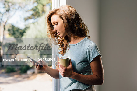 Young woman at patio door looking at smartphone