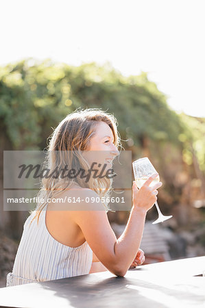 Young woman sitting outdoors, drinking from wine glass, smiling