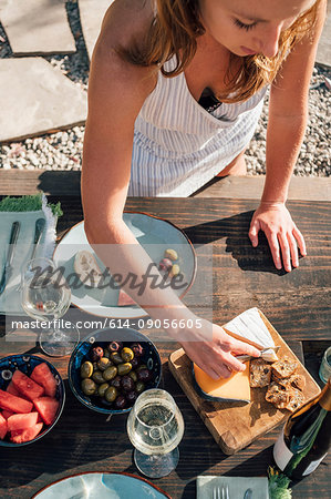 Young woman, outdoors, slicing cheese from cheeseboard, elevated view