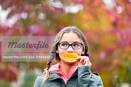 Portrait of girl with plaits and glasses covering mouth with leaf looking away