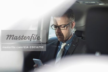 Businessman sitting in back of car, holding smartphone