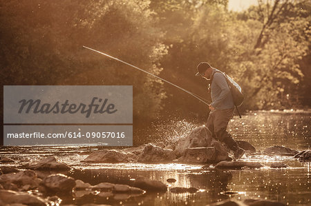 Fisherman stepping ankle deep in sunlit river, Mozirje, Brezovica, Slovenia