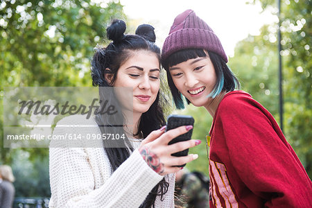 Two young stylish women looking at smartphone in city park