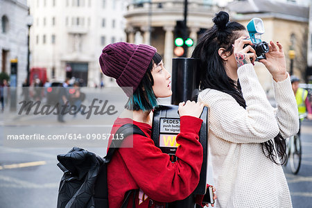 Two young stylish women taking photographs on street, London, UK