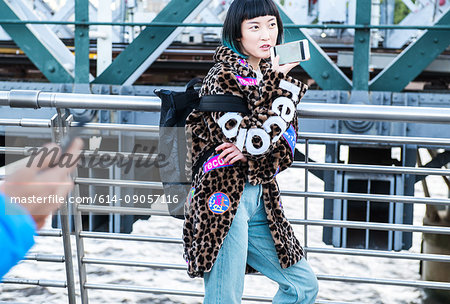 Stylish young woman making smartphone call while strolling on millennium footbridge, London, UK