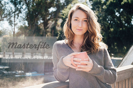 Portrait of young woman outdoors, leaning on fence, holding coffee cup