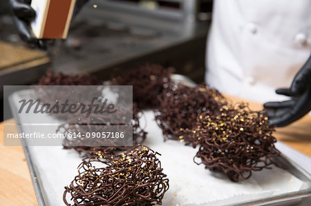 Chef sprinkling chocolate nest cake decoration with gold cake decoration