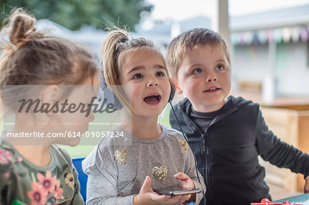 Young girl with friends, using smartphone, wearing headphones