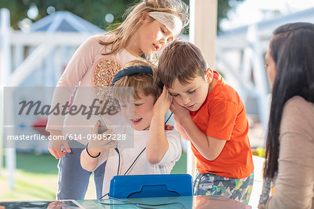 Three young children, using smartphone, listening through headphones