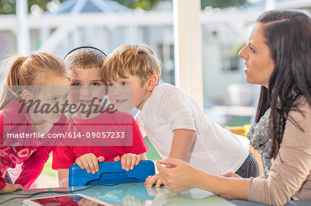Mid adult woman sitting with three young children, young boy holding digital tablet, wearing headphones