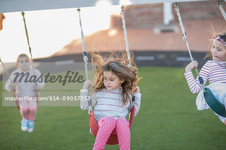 Girls at preschool, swinging on playground swings in garden