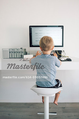 Rear view of boy at desk typing on computer