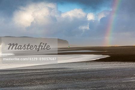 A man is walking towards the rainbow on the beach of Reynisfjara, Vik, Sudurland, Iceland, Europe