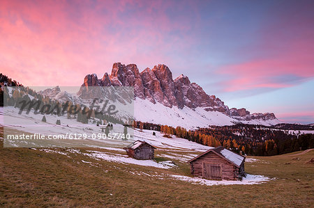 Sunrise with two wooden lodges and Odle Dolomites. Malga Gampen, Funes, Bolzano, Trentino Alto Adige - Sudtirol, Italy, Europe.