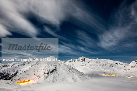 The dam and the houses in the village of Montespluga,lighted by the full moon in a winter night,Valchiavenna.