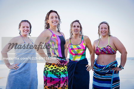 Portrait confident, smiling female open water swimmers wrapped in towels