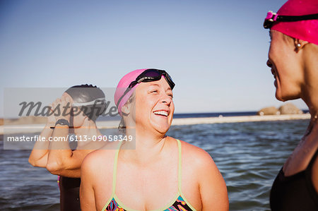 Laughing female open water swimmers talking at sunny ocean