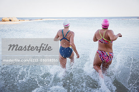 Female open water swimmers running and splashing in ocean surf