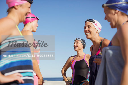 Smiling female open water swimmers talking on sunny beach