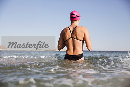 Female open water swimmer wading in sunny ocean surf