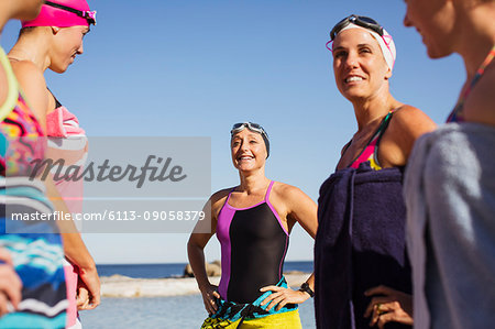 Smiling female open water swimmers wrapped din towels on sunny beach