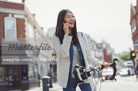 Smiling young woman commuting on bicycle, talking on cell phone on sunny urban street