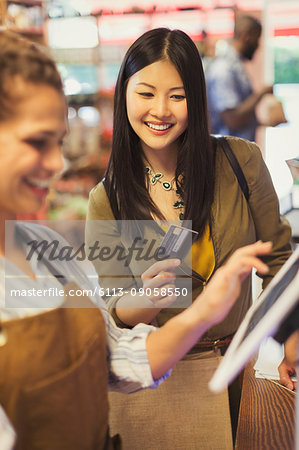 Female cashier helping smiling customer with credit card at grocery store cash register