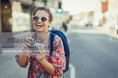 Portrait laughing, enthusiastic young female tourist in sunglasses photographing with camera on urban street