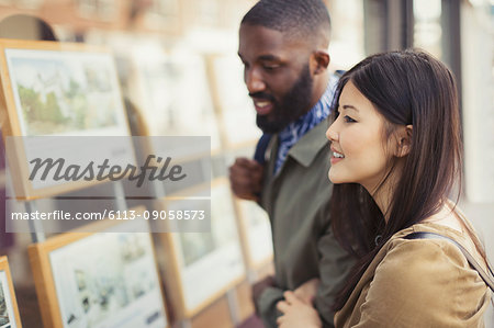 Smiling young couple looking at real estate listings at storefront Smiling young couple looking at real estate listings at storefront