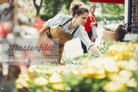 Female florist checking plants at sunny flower shop storefront