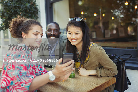 Young friends using cell phone at sidewalk cafe