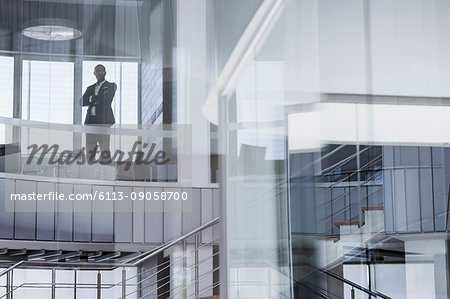 Confident CEO businessman standing with arms crossed at modern office window