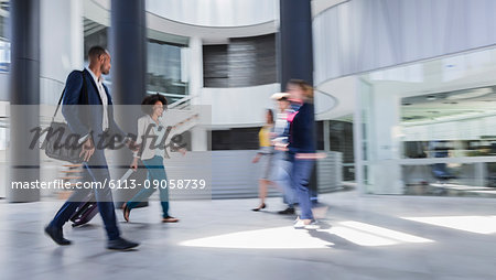 Business people walking, pulling suitcase in modern office lobby