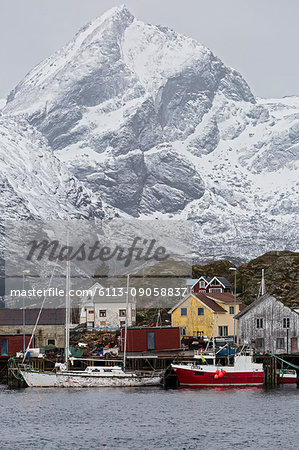 Fishing village and boats at waterfront below snowy, rugged mountains, Sund, Lofoten, Norway