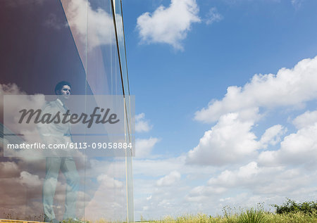 Pensive businessman looking out modern office window at sunny blue sky and clouds