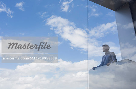 Pensive businessman standing at modern balcony looking at sunny blue sky and clouds