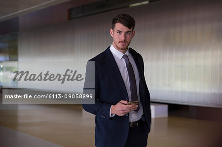 Portrait confident, serious businessman texting with smart phone in office lobby