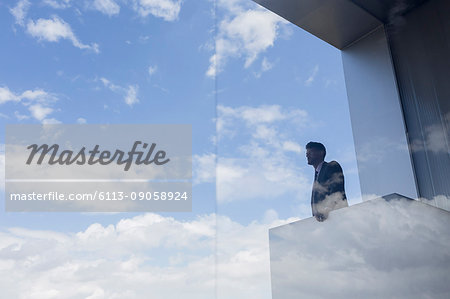 Pensive businessman on modern balcony looking at blue sky and clouds