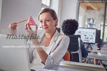 Smiling female design professional examining triangle prototype at laptop in office