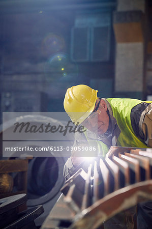 Focused steelworker with flashlight examining steel part in steel mill