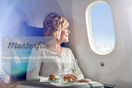 Smiling woman drinking champagne, traveling first class, looking out airplane window