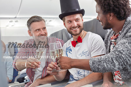 Young male friends toasting champagne glasses on airplane