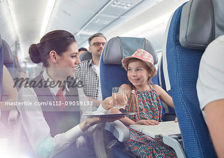 Female flight attendant serving water to girl on airplane