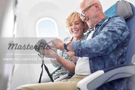 Mature couple looking at photos on digital camera on airplane