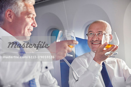 Businessman toasting whiskey glasses in first class on airplane