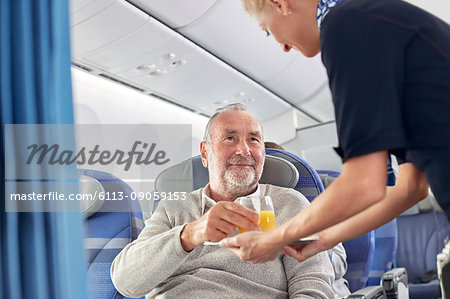 Flight attendant serving orange juice to man on airplane