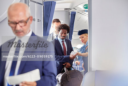 Flight attendant helping businessman with boarding pass on airplane