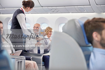 Flight attendant serving whiskey to businessman in first class on airplane