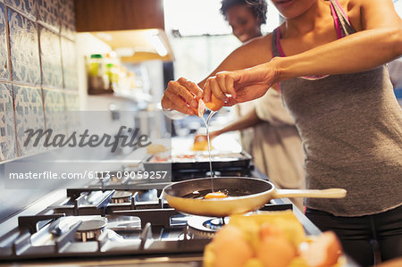 Young woman cracking egg over skillet on stove in kitchen