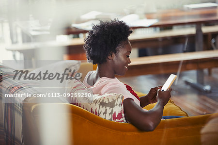 Smiling woman texting with smart phone on living room sofa